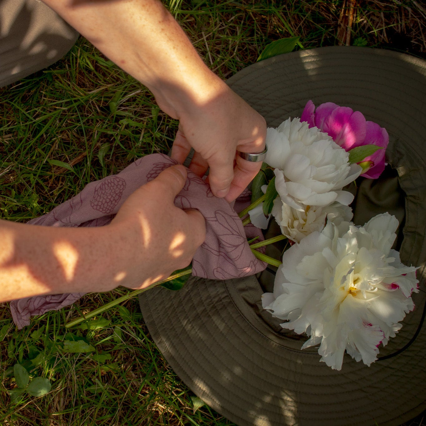 Person arranging flowers on a hat in a grassy area