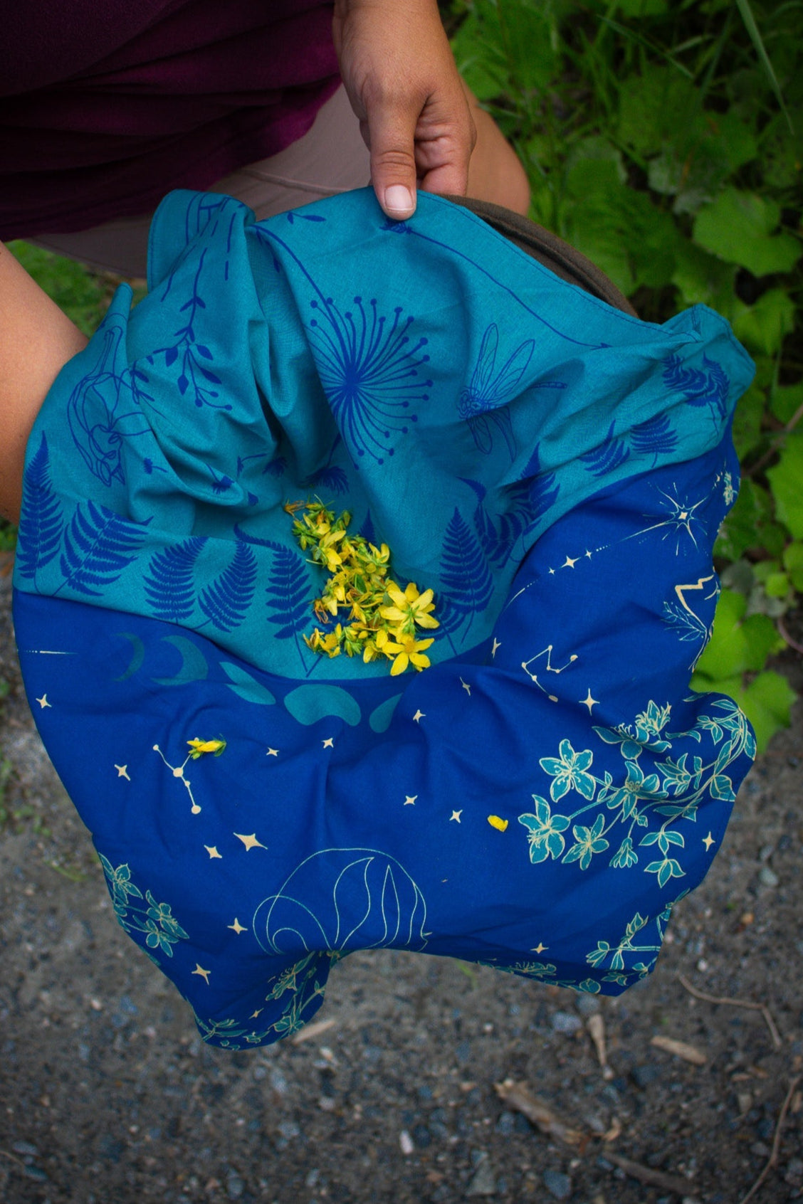 Blue floral bandana with st johns wort held by a person with greenery in the background