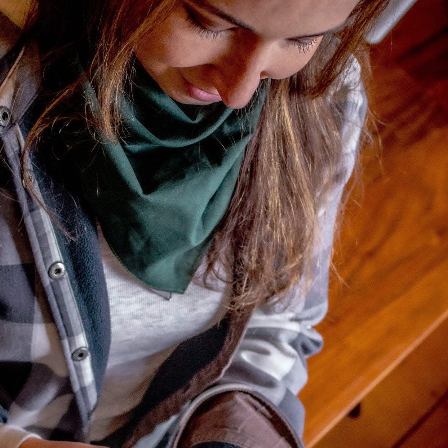Person holding a red container with a label, wearing a plaid shirt and green scarf indoors.
