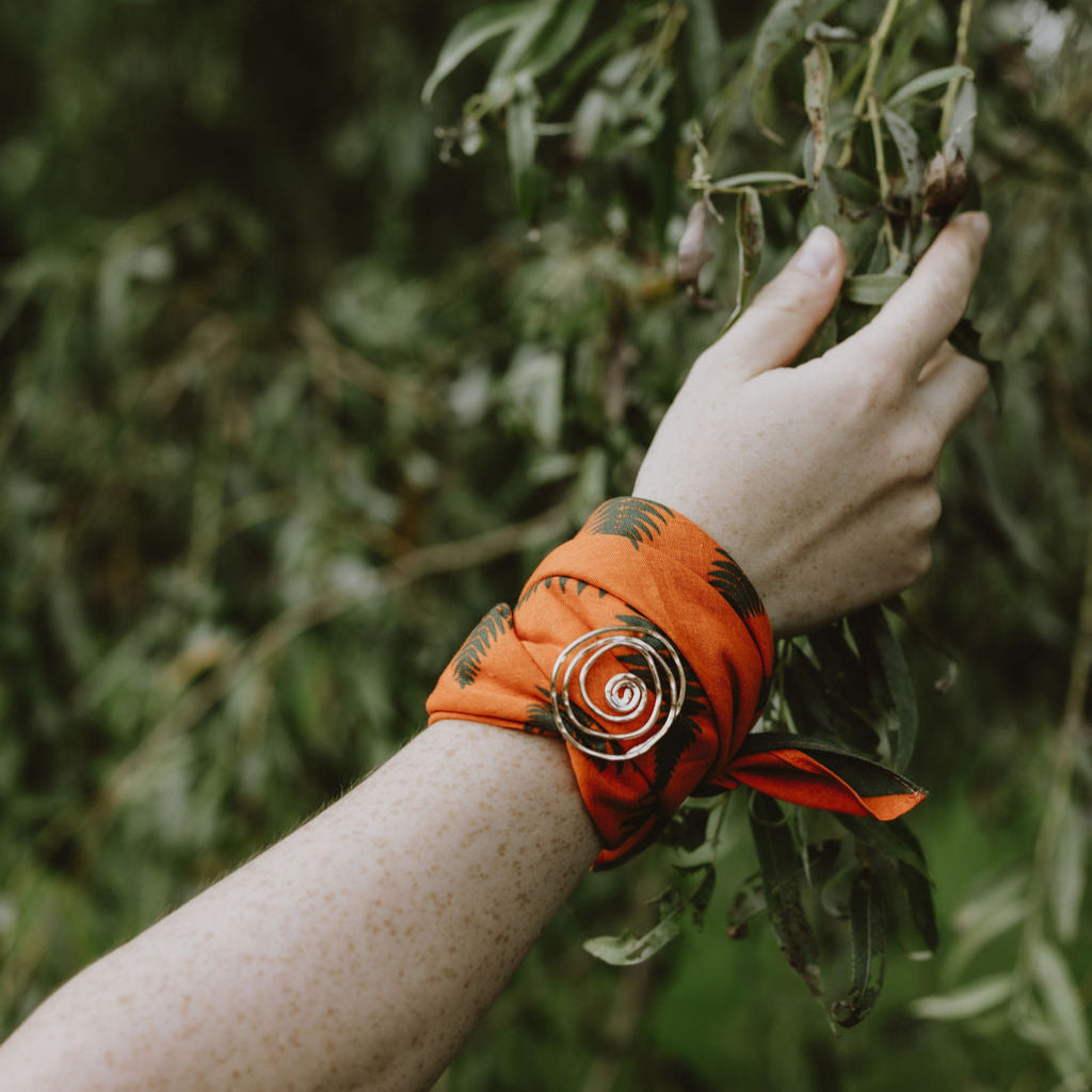 Hand with orange bracelet touching a tree branch in a forest setting