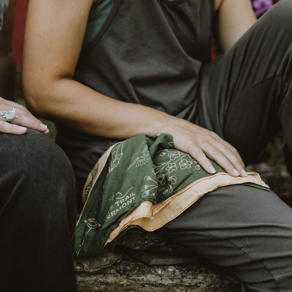 woman sitting on stone wall with romper and green and yellow off trail vermont bandana split