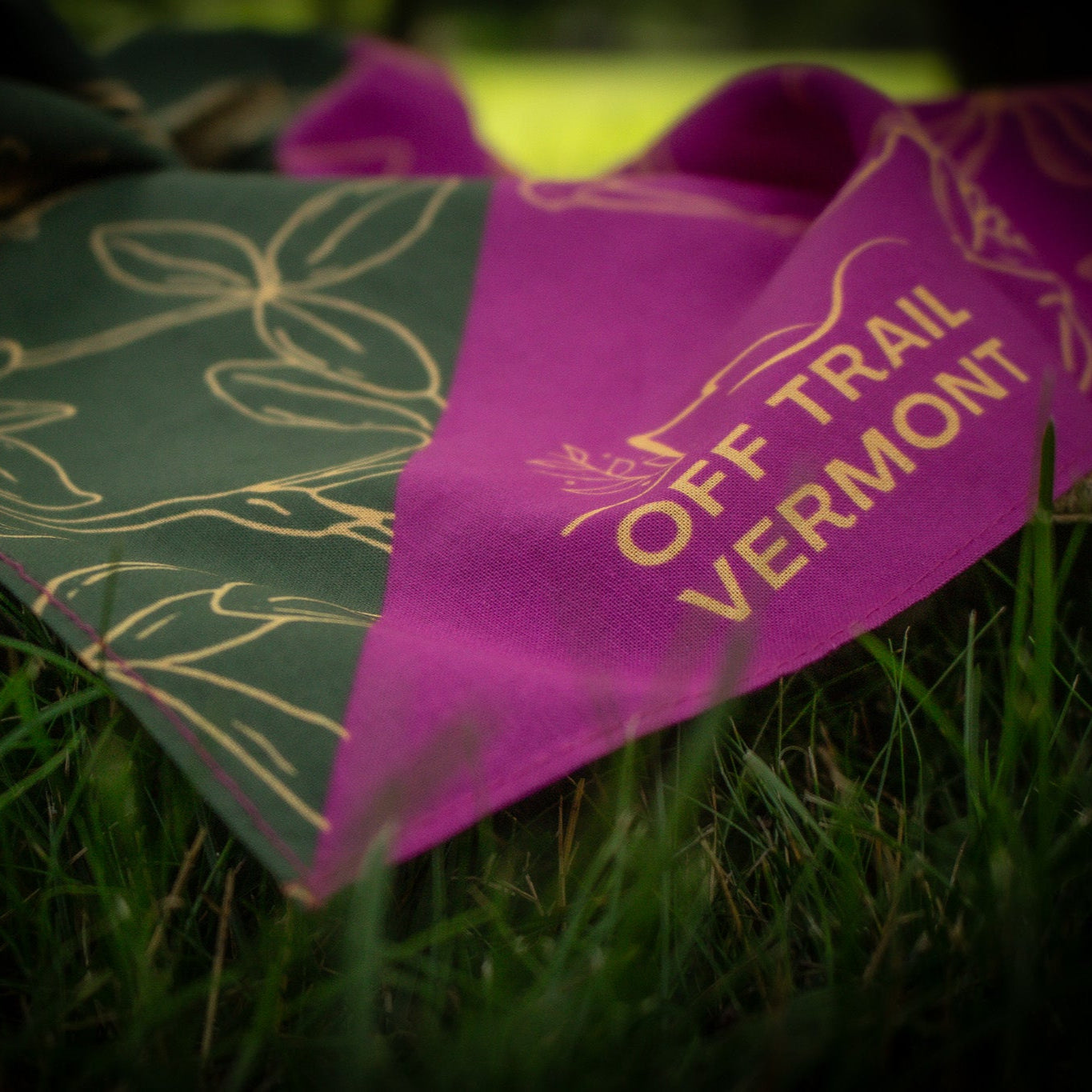 Pink and green bandana with off Trail Vermont logo on the grass