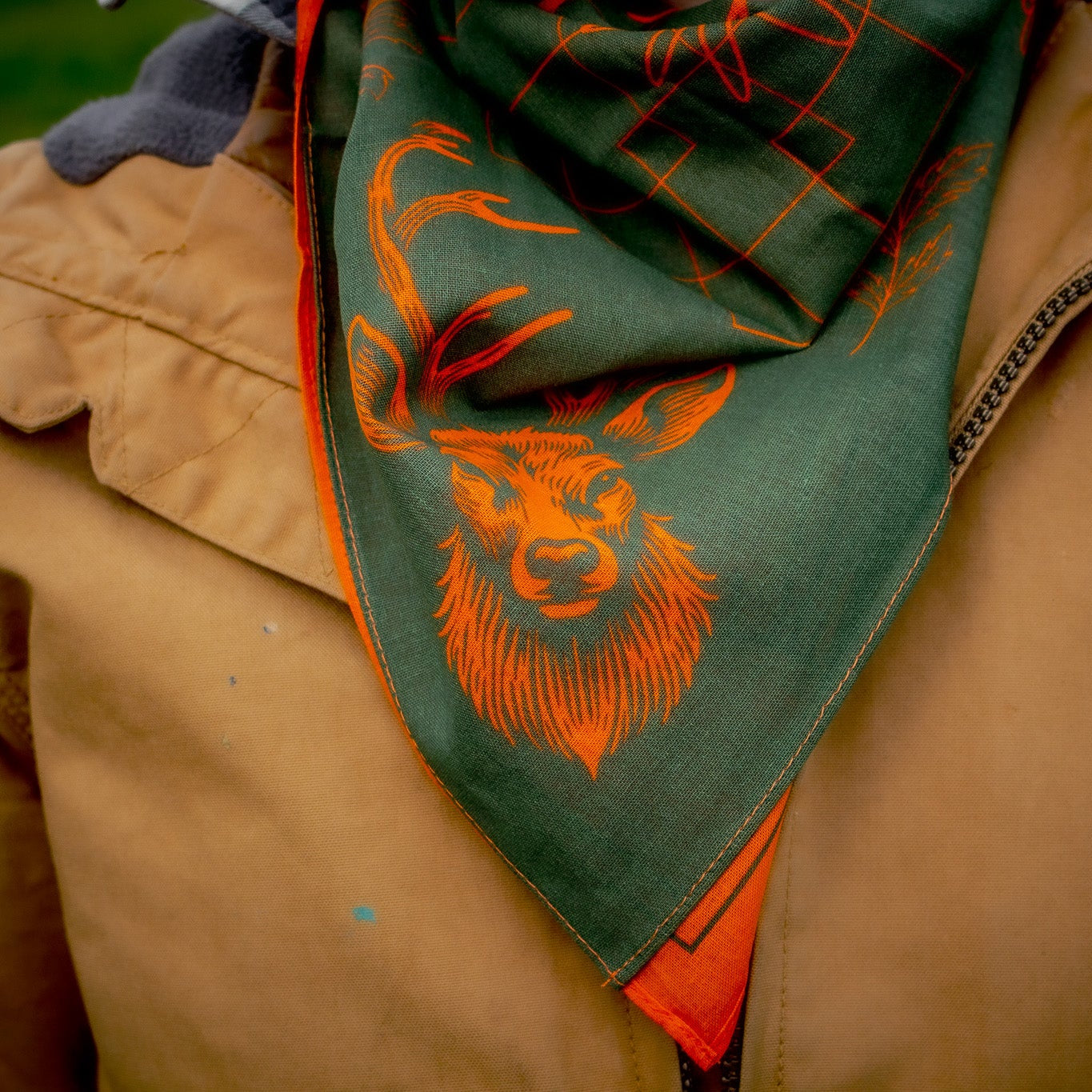 Person wearing a green and orange patterned scarf with a deer design on a brown jacket.