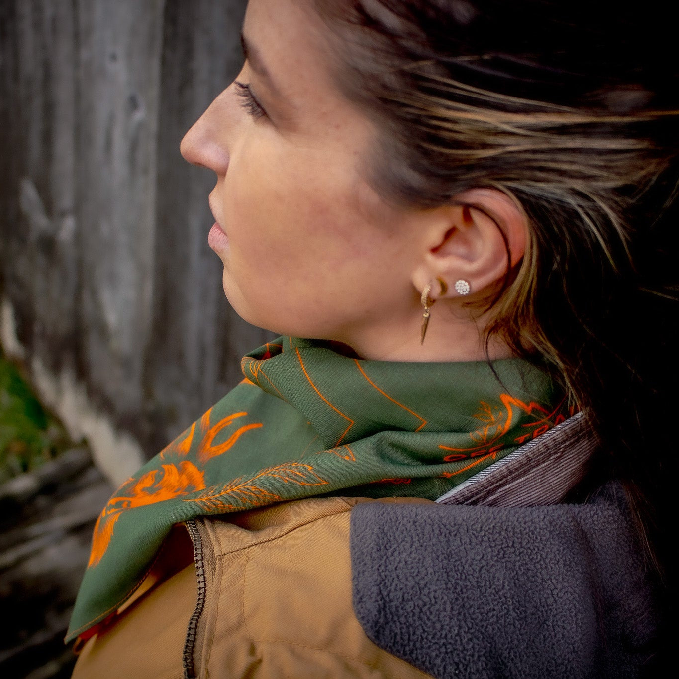 Woman wearing a green scarf with orange deer patterns, standing against a textured wall.