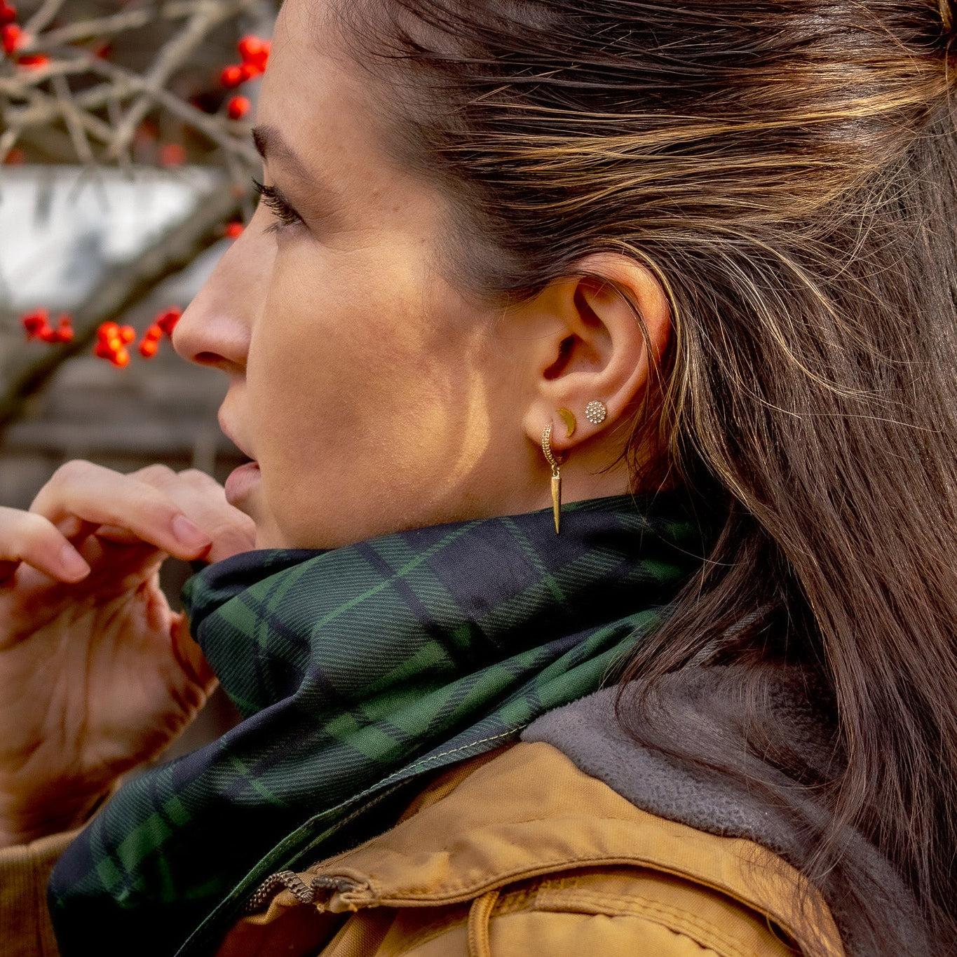 Woman wearing a freen plaid scarf with a blurred background of red berries and wooden structures