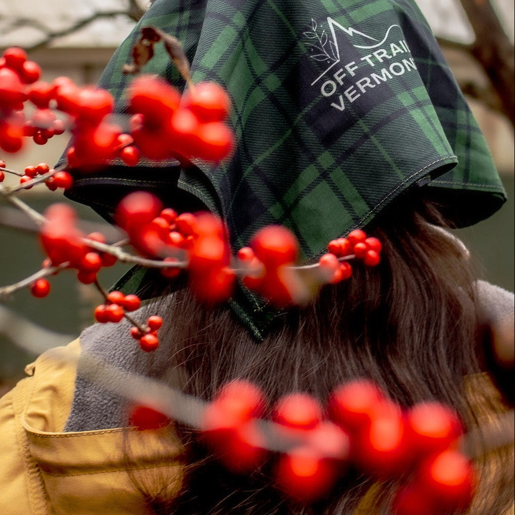 Person wearing a green plaid cap with 'Off Track Vermont' logo, surrounded by red berries.