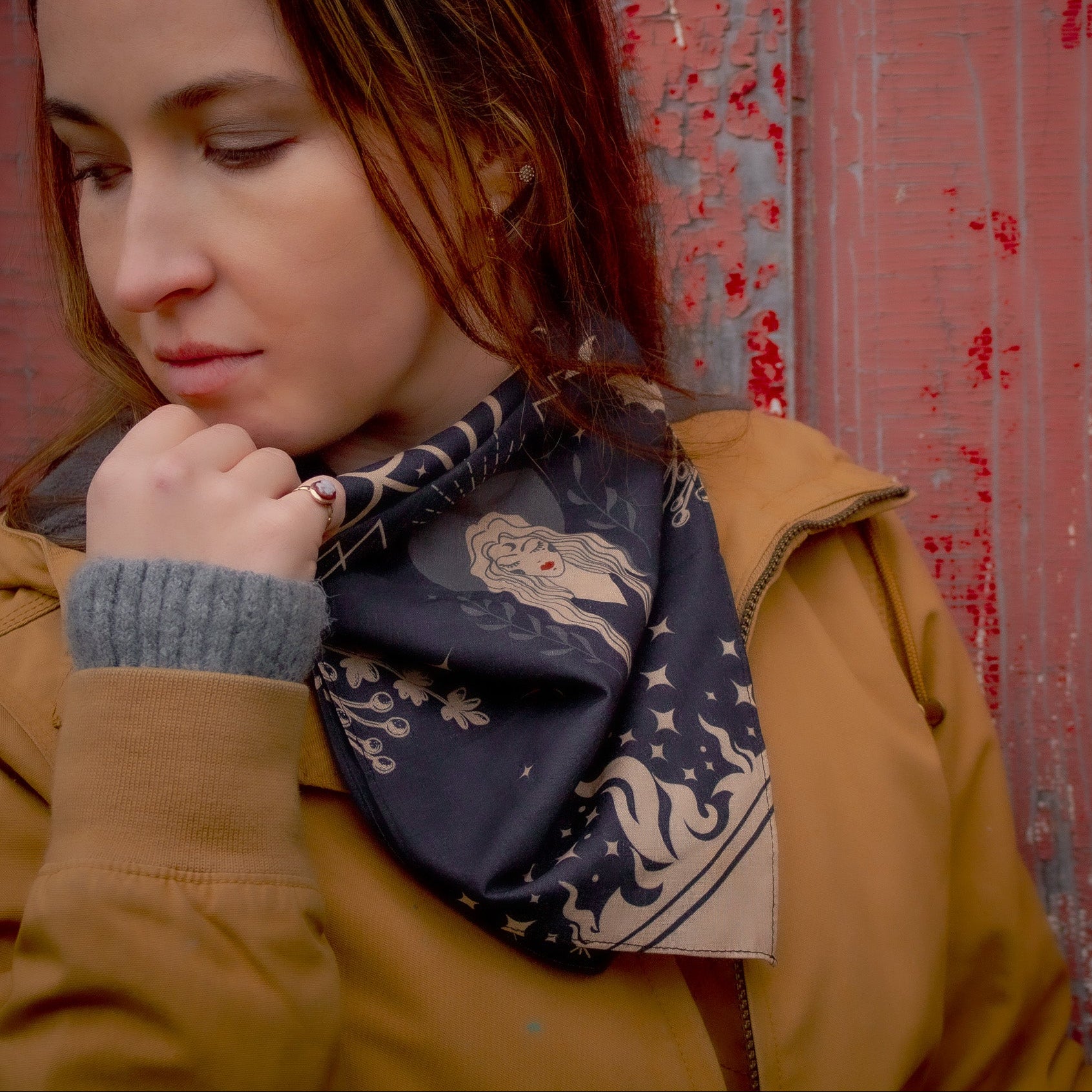 Woman wearing a black and tan full moon scarf against a textured red wall