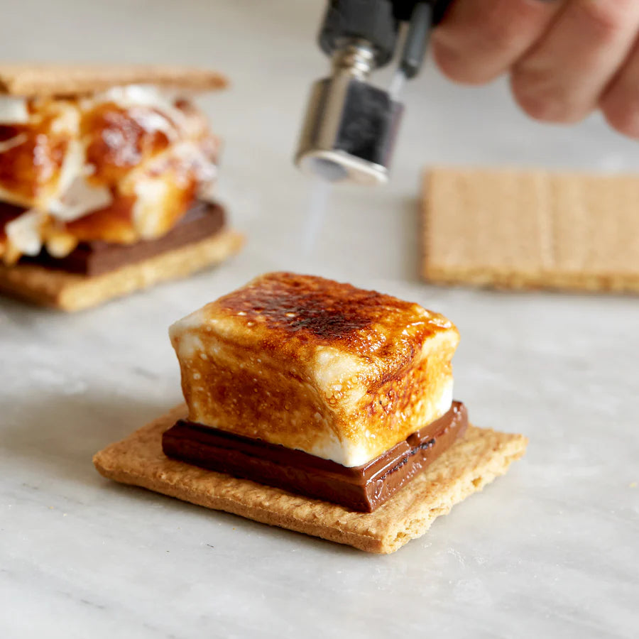 VERMONT made marshmallow S'mores being prepared with a marshmallow being toasted over a flame.