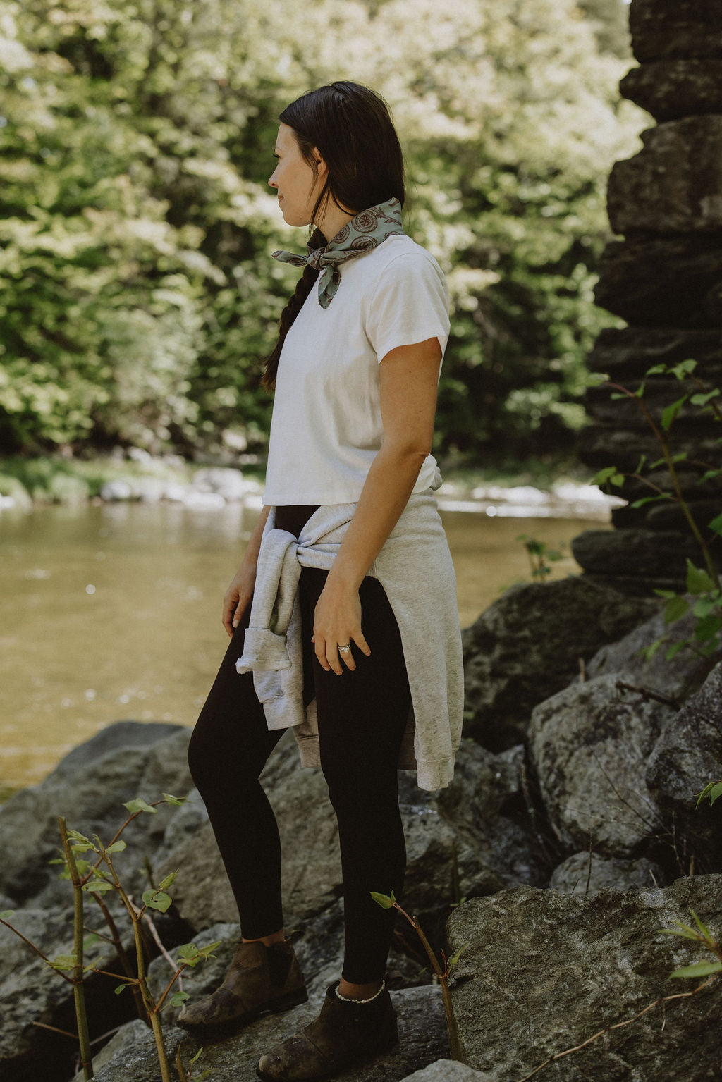 woman standing on rocks by river with fiddlehead bandana on neck
