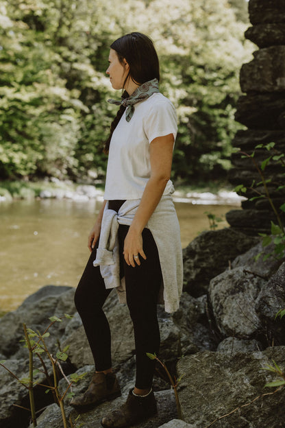 woman standing on rocks by river with fiddlehead bandana on neck