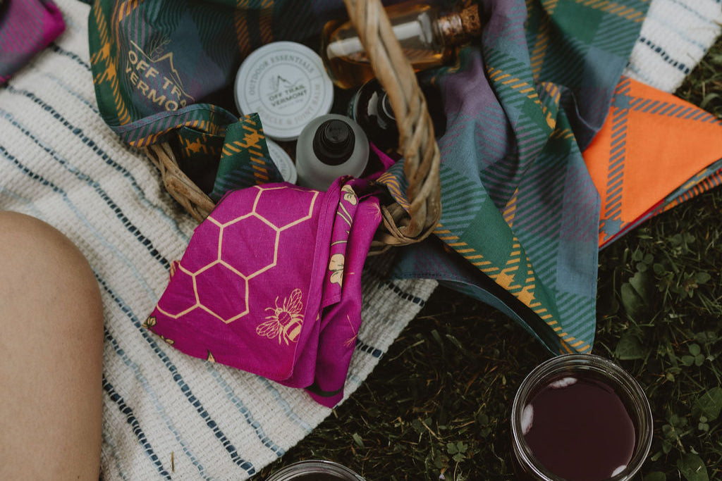 Basket with plaid fabric, feather, and small items on a blanket with books and cups.