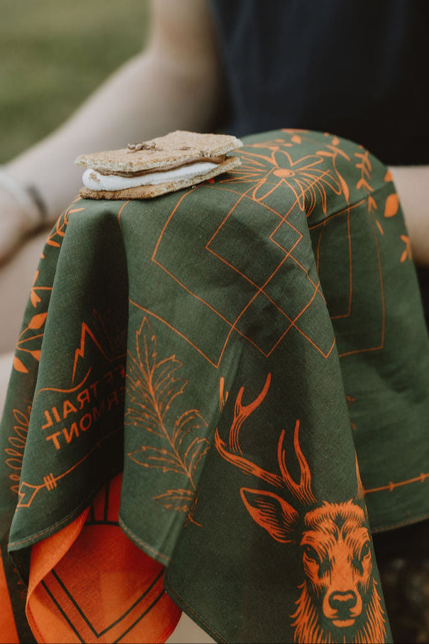 Person sitting outdoors with a green towel featuring deer designs.