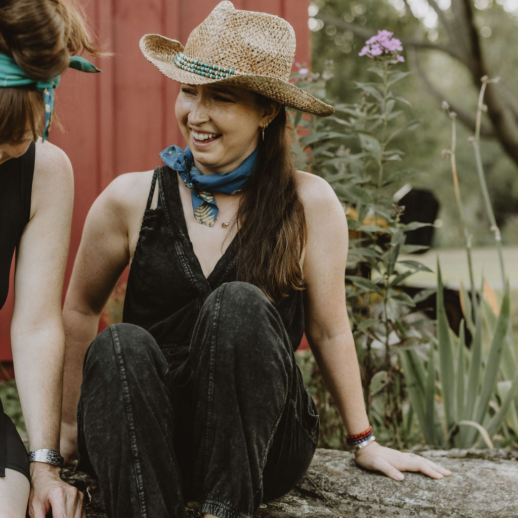 woman laughing on a stone wall with blue defiance bandana and cowboy hat
